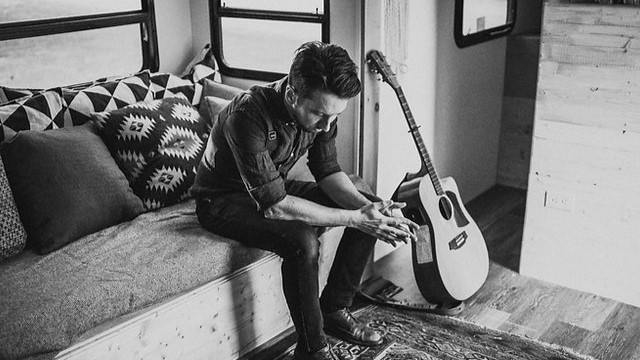 Jay sitting on a bench with his guitar